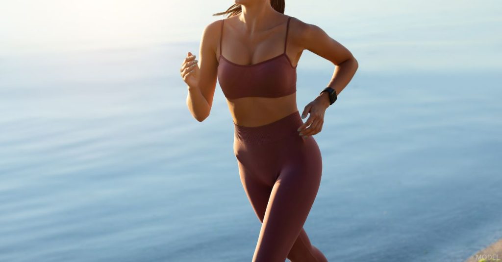 Woman wearing leggings and sports bra on a run near the ocean (model)